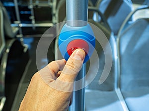 The finger of an adult person`s hand presses the stop button for the bus stop. Red button