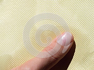 Finger on bulletproof material aramid. Shining aramid kevlar background. Yellow kevlar texture and pattern