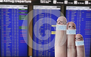 Finger face family with masks in front of flight timetable on airport