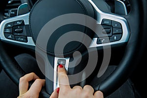 The finger of a female hand points to the heated steering wheel button on the multifunction steering wheel, the