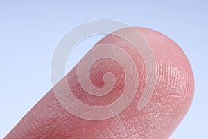 Finger with friction ridges on light blue background, macro view