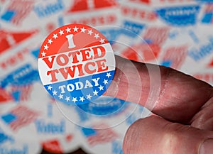 Finger with I Voted Twice sticker in front of many election voting badges to illustrate voter fraud