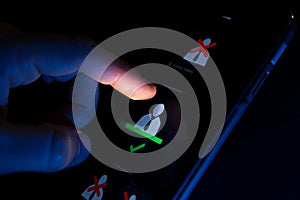 A finger interacts with a smartphone screen, selecting an icon of a person with a green checkmark beneath it