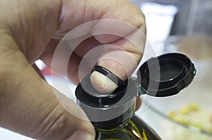 Finger opening a sealed olive oil bottle with an inner pull-off plastic tab underneath the cap
