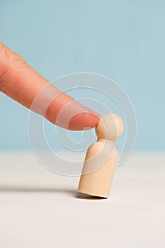 A finger pokes into a wooden figure on a blue background. Concept fired. Staff reduction. Close up