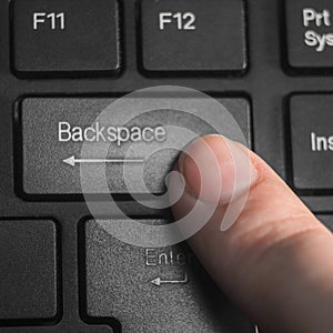 A finger pressing the `Backspace` key on the black keyboard