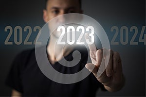 Finger pressing blue start 2023 button on virtual interface on gray background with copy space for text. Concept of new