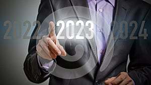 Finger pressing blue start 2023 button on virtual interface on gray background with copy space for text. Concept of new