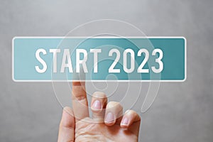 Finger pressing blue transparent start 2023 button on virtual interface on gray background with copy space for text.