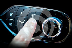 A finger pressing the A/C or air conditioning button on the dashboard of a car photo