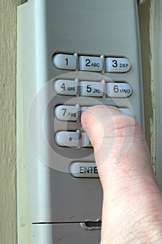 finger pushing buttons for secret code on Garage door keypad on a home for security