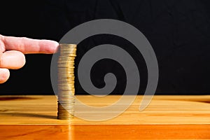 Finger pushing a column of coins on wooden table with black wall