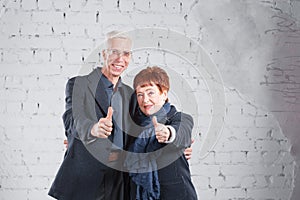 Finger to the top, like. Happy smiling old couple standing cuddling together isolated on white brick background. copy