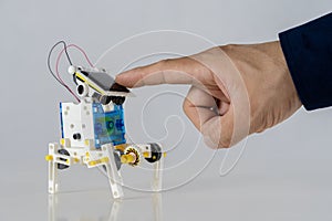 A finger touches a solar panel above a toy robot made from plastic packaging. Sustainable technology education concept