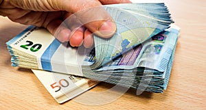 Fingers flicking through a stack of ten Euro bills, with another stack of fifties