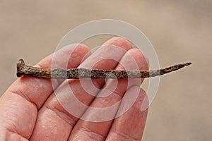 Fingers on the hand holds one brown rusty iron nail