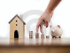 Fingers hand step forward on stack of coins with piggy bank and model house on white space background concept business finance