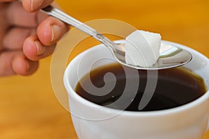 Fingers hold spoon with lump sugar piece over cup