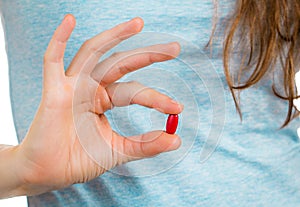 Fingers holding a red pill.