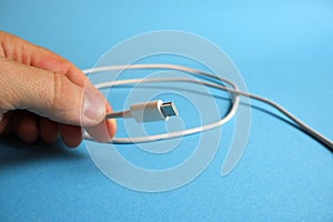 Fingers are holding a white usb cable with a type c interface on a blue background.