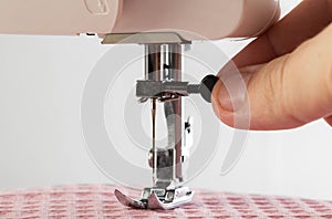 The fingers of a seamstress unscrew the needle holder of a sewing machine needle, close-up. Copy space for text