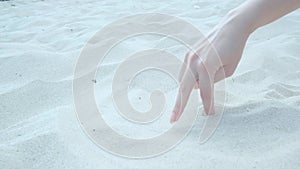 The fingers of a woman's hand walk along the sand on the beach