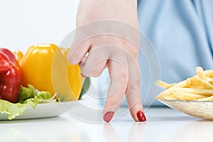 Fingers of a young lush fat woman in casual blue clothes on a white background, the choice between healthy food and fast