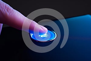 fingertip contacting a glowing blue start button on a gadget