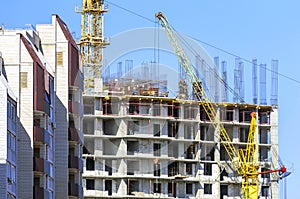 Finished Apartment Building and a New High-Rise Building Construction Site with Yellow Cranes against Blue Sky. Real Estate,