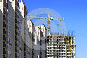 Finished Apartment Building and a New High-Rise Building Construction Site with Yellow Cranes against Blue Sky. Real Estate,