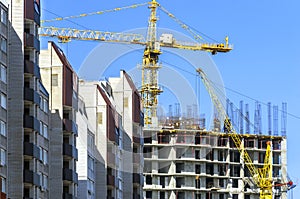 Finished Apartment Building and a New High-Rise Building Construction Site with Yellow Cranes against Blue Sky. Real Estate,