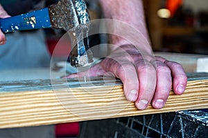 Finishing nail being driven in with a hammer while a hand supports the board