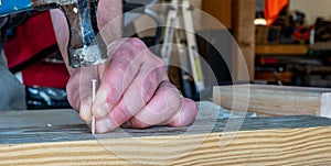 Finishing nail being driven in with a hammer while a hand supports the board