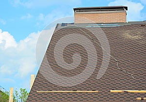 Finishing tiling, installing asphalt shingles on underlayment at the ridge of the rooftop near the brick chimney