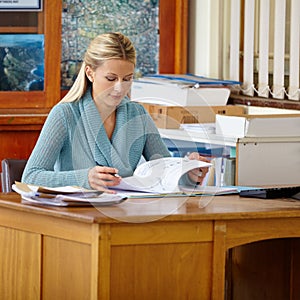 Finishing up her days work. A young teacher marking classwork and tests at her classroom desk.