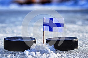 Finská vlajka na párátku mezi dvěma hokejovými puky. Finsko bude hrát na Světovém poháru ve skupině A. 2019 IIHF World Championship