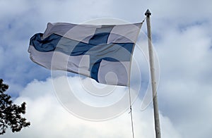 Finnish flag hoisted in a handmade flagpole against white clouds