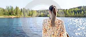 Finnish woman standing and looking at a lake in Finland. Happy person relaxing and enjoying sunny summer vacation or weekend.