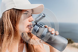 Fintess woman drinking water. Happy, active middle aged woman standing on beach and drinking water after excersise