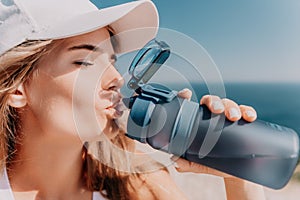 Fintess woman drinking water. Happy, active middle aged woman standing on beach and drinking water after excersise