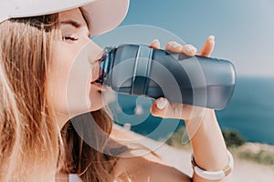 Fintess woman drinking water. Happy, active middle aged woman standing on beach and drinking water after excersise