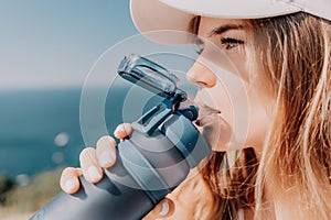 Fintess woman drinking water. Happy, active middle aged woman standing on beach and drinking water after excersise