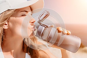 Fintess woman drinking water. Happy, active middle aged woman standing on beach and drinking water after excersise