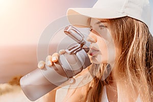 Fintess woman drinking water. Happy, active middle aged woman standing on beach and drinking water after excersise