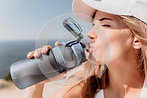 Fintess woman drinking water. Happy, active middle aged woman standing on beach and drinking water after excersise