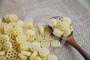 Fiori raw pasta in wooden spoon on sack rustic background . Natural and healthy food concept. Flower shape.