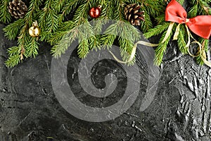 Fir branch with balls, gifts, pine cone and bows on a black wooden background