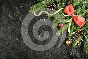 Fir branch with balls, gifts, pine cone and bows on a black wooden background