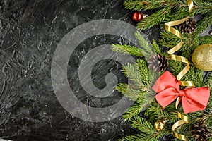 Fir branch with balls, gifts, pine cone and bows on a black wooden background