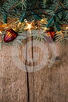 Fir branch with Christmas decorations and glowing garland on old wooden background with empty space for text. Top view